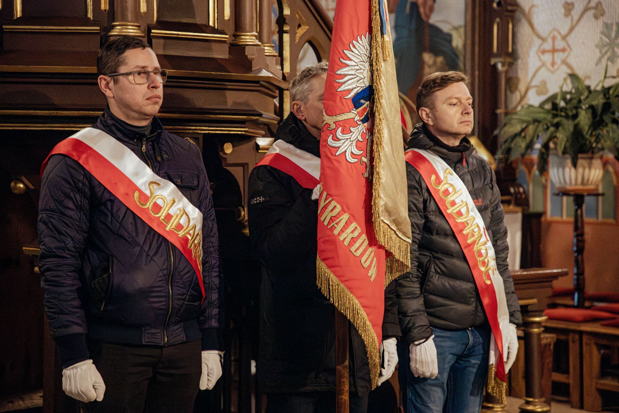 Trójka mężczyzn stojąca ze sztandarem "Solidarności"