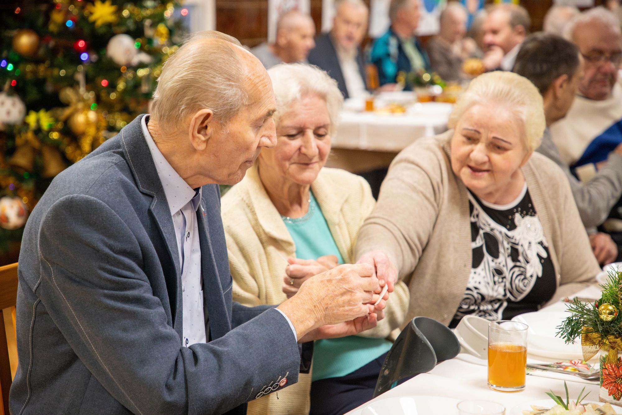 Seniorzy przy stole dzielą się opłatkiem